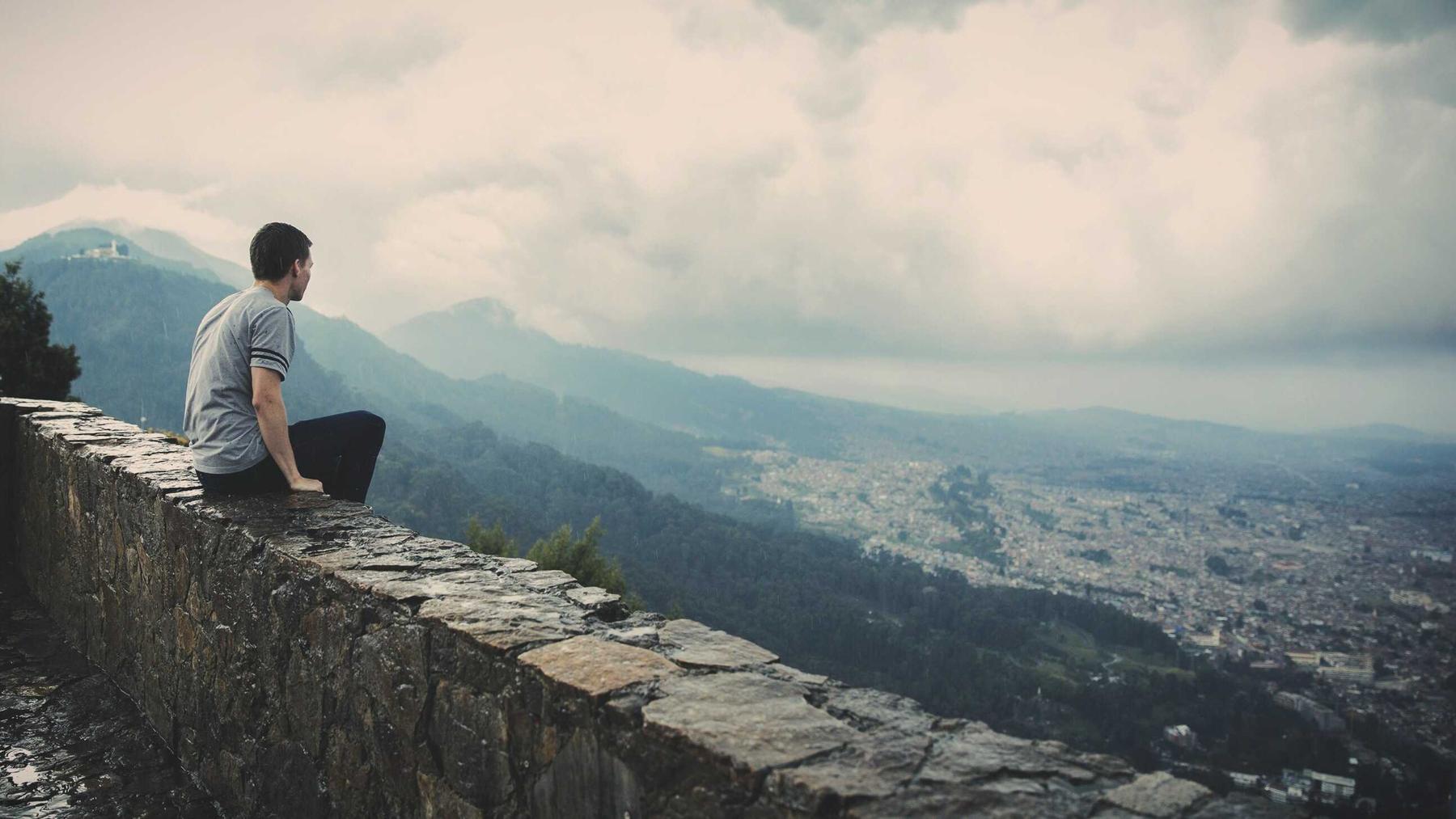 A person sitting on a stone wall above a valley, cloud sitting low over the far hills.